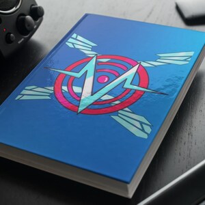 May include: A blue notebook with a graphic design on the cover. The design features a white and light blue lightning bolt shape inside a red and pink circle, with light blue wing shapes. The notebook is on a dark surface.
