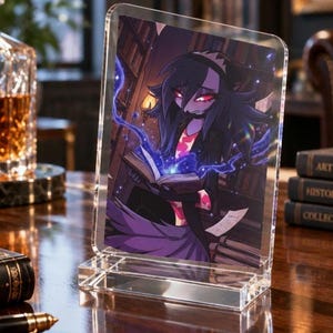 May include: A clear acrylic stand holding a rectangular print featuring an animated character with dark hair and red eyes reading a glowing book. The character wears a dark outfit with pink accents, set against a library background with shelves.