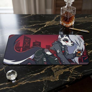 Op de afbeelding: Een rechthoekige muismat met een cartoon wolf karakter en een stadslandschap achtergrond. Het karakter draagt een zwarte outfit en houdt een blikje met het opschrift "Hellfire" vast. De achtergrond is rood.