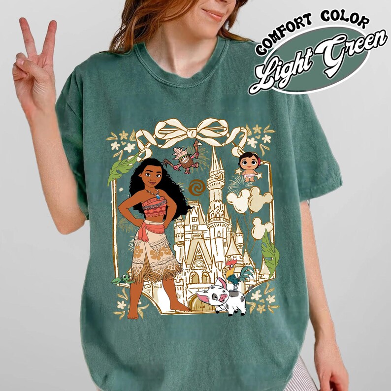 May include: Light green t-shirt with a graphic of a cartoon character in a floral frame. The graphic includes a castle, a pig, and other characters. The text "COMFORT COLOR Light Green" is on the upper right.