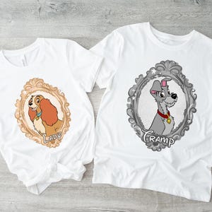 K&ouml;nnte beinhalten: Zwei wei&szlig;e T-Shirts mit Cartoon-Hundeportr&auml;ts in verzierten Rahmen. Eines zeigt einen braunen und beigen Hund mit dem Namen "Lady", das andere einen grauen Hund mit dem Namen "Tramp".