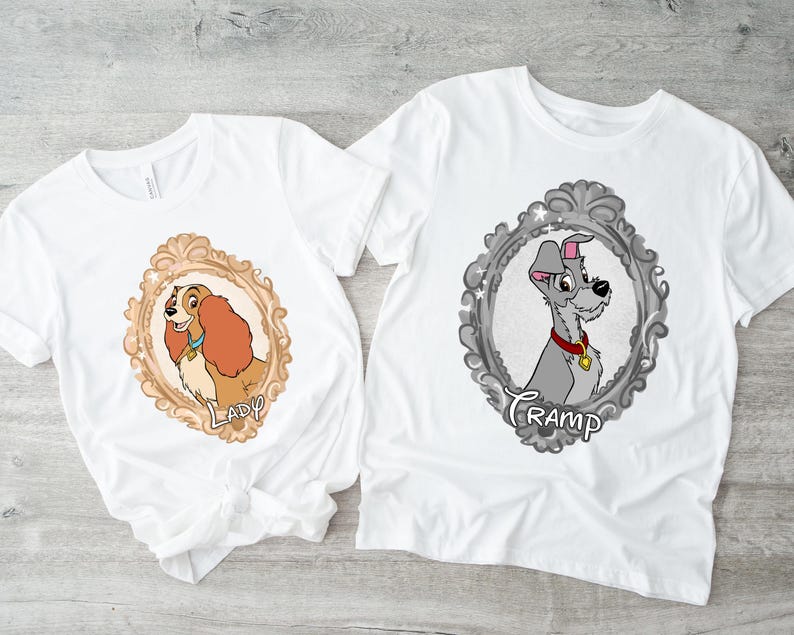 K&ouml;nnte beinhalten: Zwei wei&szlig;e T-Shirts mit Cartoon-Hundeportr&auml;ts in verzierten Rahmen. Eines zeigt einen braunen und beigen Hund mit dem Namen "Lady", das andere einen grauen Hund mit dem Namen "Tramp".
