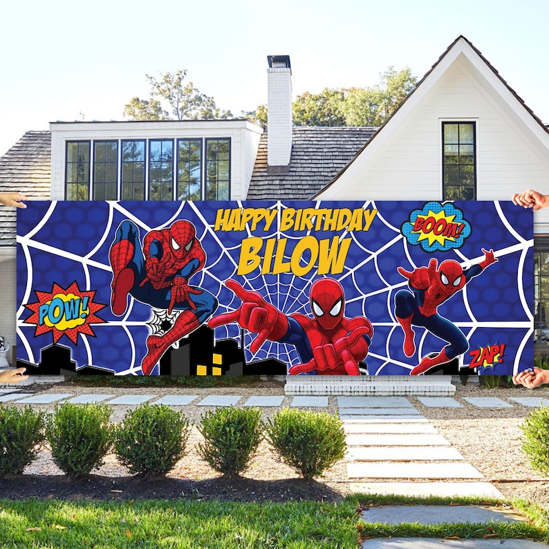 May include: A blue banner featuring Spider-Man illustrations and comic book sound effects. The banner reads "Happy Birthday Bilow" in yellow text, with a white spiderweb design in the background.