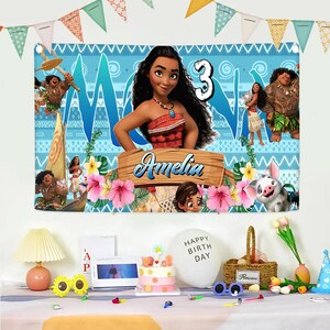 May include: A rectangular birthday banner featuring Moana characters, a large number 3, and the name Amelia on a wooden sign. The background is light blue with tribal patterns, tropical flowers, and green leaves. The banner has grommets at the top corners.