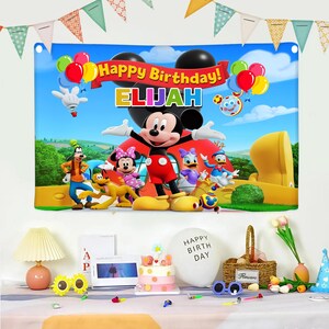 Pu&ograve; includere: Un colorato banner di compleanno con Topolino e i suoi amici, con la scritta "Happy Birthday! ELIJAH". Il banner include palloncini e uno sfondo di cielo blu, perfetto per una festa di compleanno per bambini.