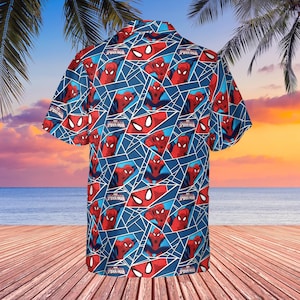 K&ouml;nnte beinhalten: Blaues kurz&auml;rmeliges Button-Down-Hemd mit einem sich wiederholenden Muster von Spider-Man in roten und blauen geometrischen Formen. Das Hemd enth&auml;lt den Text "Spider-Man" in Wei&szlig;. Das Hemd wird auf einem Holzdeck mit Strand und Sonnenuntergang im Hintergrund pr&auml;sentiert.