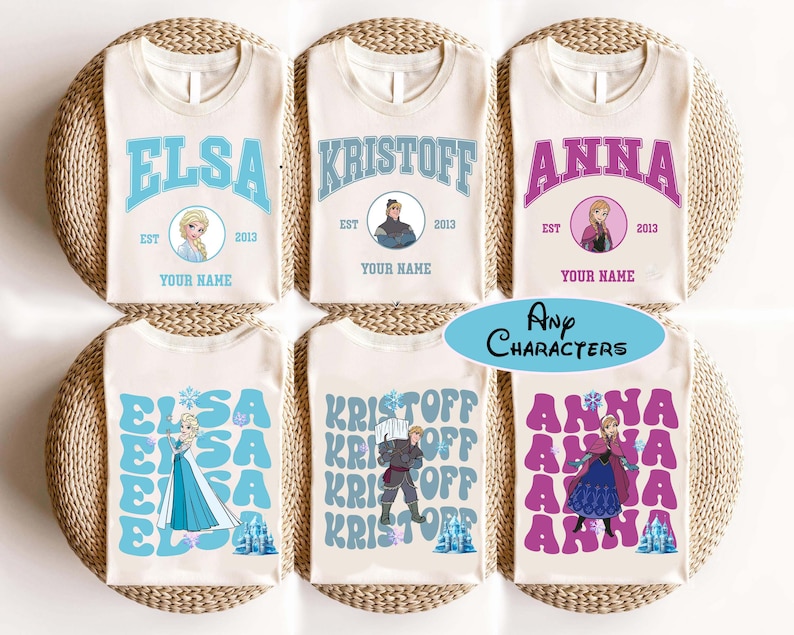 Puede incluir: Camisetas color crema con los nombres "ELSA", "KRISTOFF" y "ANNA" en varias fuentes y colores. Cada camiseta incluye una imagen de personaje, el a&ntilde;o "2013" y el texto "YOUR NAME". Las camisetas se muestran sobre una superficie tejida.