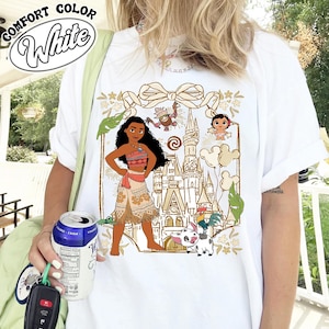May include: White t-shirt featuring a graphic of a cartoon character with a castle, characters, and the text "COMFORT COLOR White". The design includes a bow, leaves, and other characters.