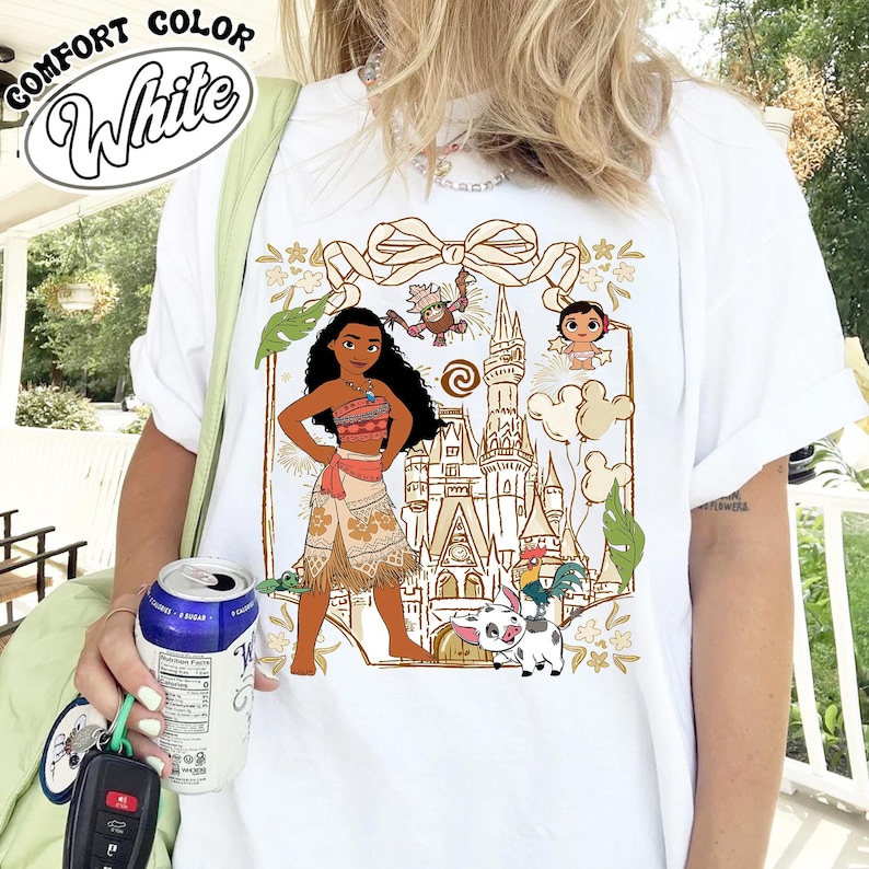 May include: White t-shirt featuring a graphic of a cartoon character with a castle, characters, and the text "COMFORT COLOR White". The design includes a bow, leaves, and other characters.