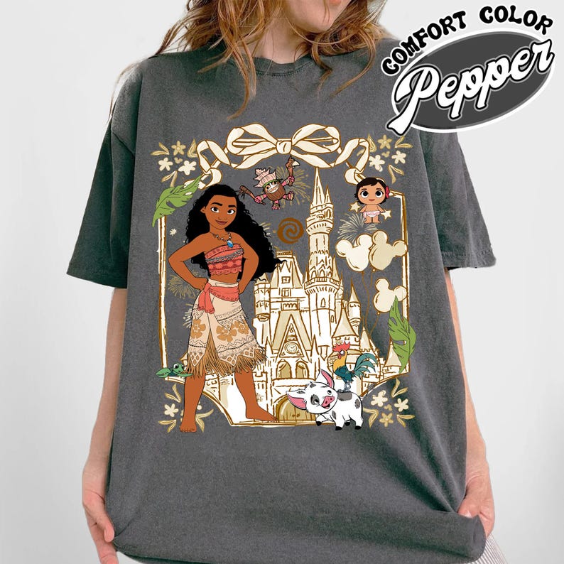May include: Dark gray t-shirt featuring a colorful graphic of a cartoon character, a castle, and other characters. The graphic is framed by a gold outline with floral and leaf accents. The words "COMFORT COLOR Pepper" are printed on the upper right.