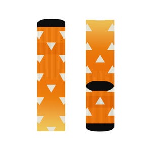 Op de afbeelding: Een paar sokken met een herhaald patroon van witte driehoeken op een oranje en gele gradiënt achtergrond. De bovenkant en de hiel van de sokken zijn zwart.