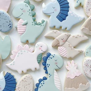 May include: An assortment of dinosaur-shaped cookies in pastel colors. The cookies include a triceratops, a stegosaurus, and a T-Rex, with details like spines, horns, and stripes. Other cookies are shaped like eggs and volcanoes.