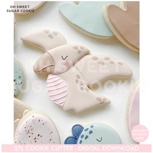May include: A collection of decorated sugar cookies in the shape of a pterodactyl, with a light beige color and brown spots. The cookies have pink and blue accents. Text on the image reads "OH SWEET SUGAR COOKIE" and "STL COOKIE CUTTER - DIGITAL DOWNLOAD."