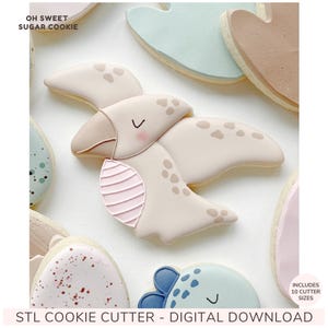 Peut inclure: Un biscuit en forme de ptérodactyle décoré de glaçage beige, de taches brunes et de détails roses, avec le texte OH SWEET SUGAR COOKIE et STL COOKIE CUTTER - DIGITAL DOWNLOAD. Le biscuit présente un œil fermé et une aile texturée.