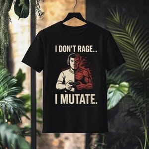 May include: Black t-shirt with the text "I DON'T RAGE... I MUTATE." The graphic shows a gamer with headphones, split into two halves: one normal, the other transformed with red muscle. The shirt is hanging on a black hanger.