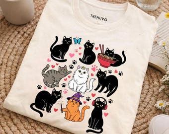 May include: Cream-colored t-shirt with a graphic of various cartoon cats. The cats are in different poses and colors, including black, gray, orange, and white. Some cats have accessories like crowns, headphones, and wizard hats. The brand name "TRENUVO" is printed on the collar.