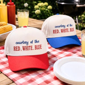 Può includere: Due cappellini da baseball con corona color bianco sporco e testo ricamato che recita "courtesy of the RED, WHITE, BLUE". Un cappellino presenta una visiera rossa tinta unita, l'altro una visiera blu tinta unita, entrambi con bottone.