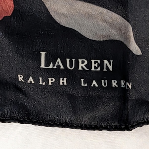 May include: Close-up of a black silk scarf with a floral design in shades of red and gray. The scarf features the text "LAUREN RALPH LAUREN" in white lettering.