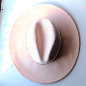 Może przedstawiać: Jasnor&oacute;żowy kapelusz typu fedora z szerokim rondem. Kapelusz ma zaokrągloną koronę i kremową opaskę. Kapelusz wykonany jest z miękkiego materiału i nadaje się na r&oacute;żne okazje. Średnica ronda wynosi około 30 cm.