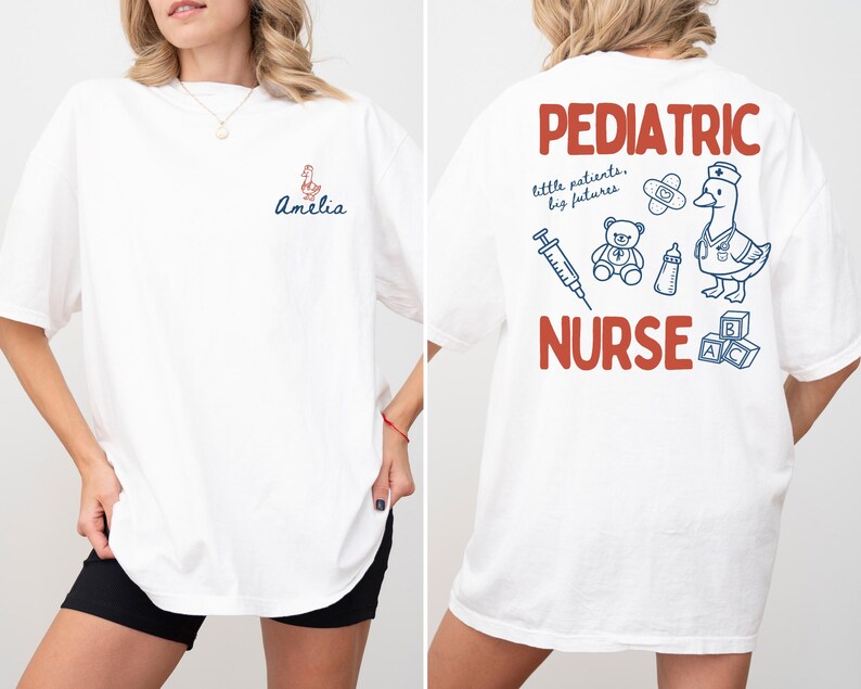 Puede incluir: Camiseta blanca con "Amelia" y un gr&aacute;fico de pato en la parte delantera. La parte trasera presenta "Pediatric Nurse" en texto rojo, junto con ilustraciones de un pato, un oso de peluche y suministros m&eacute;dicos en azul.