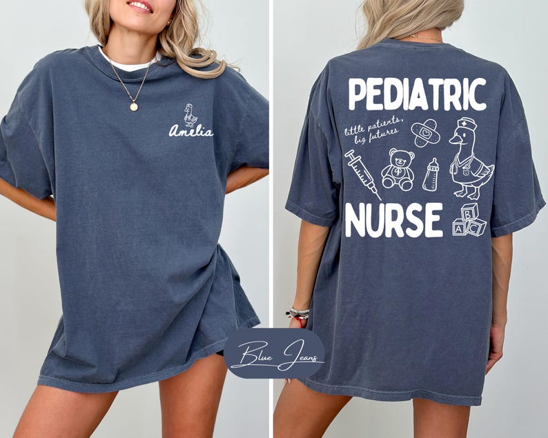 Puede incluir: Camiseta azul oscuro con la frase "Pediatric Nurse" e ilustraciones m&eacute;dicas, adem&aacute;s de un pato con gorro de enfermera. La parte delantera muestra el nombre "Amelia" y un peque&ntilde;o dibujo de pato.