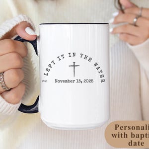 May include: White ceramic mug with a black handle and rim. The mug features the text "I LEFT IT IN THE WATER" in a semi-circle above a cross symbol and the date "November 15, 2025". The mug is designed to be personalized with a baptism date.