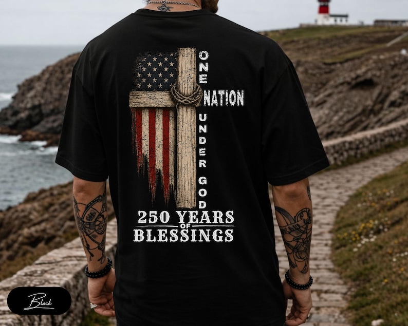 May include: A black t-shirt featuring a graphic on the back. The design displays a wooden cross overlaid with a distressed American flag, a crown of thorns, and the text ONE NATION UNDER GOD 250 YEARS OF BLESSINGS in white capital letters.