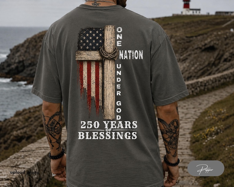 May include: A charcoal gray t-shirt featuring a back graphic of a distressed American flag integrated with a wooden cross and a crown of thorns. The text reads ONE NATION UNDER GOD and 250 YEARS OF BLESSINGS in a white, weathered, serif font.