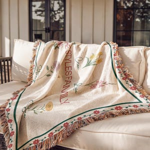 May include: Cream-coloured throw blanket with floral designs and the text "THE STYLES FAMILY" in red. The blanket has a green border with red flowers and fringe.