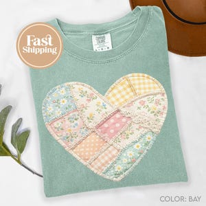 Peut inclure: T-shirt vert clair Comfort Colors avec un motif de cœur en patchwork. Le cœur est composé de divers tissus floraux et à motifs aux couleurs pastel. Le t-shirt a un col rond et des manches courtes. Le texte "Fast Shipping" est dans un cercle à gauche.