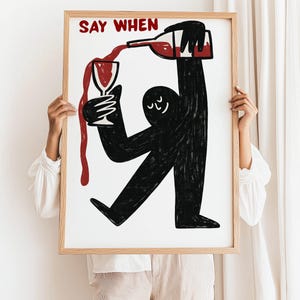 May include: A framed art print with a whimsical illustration of a figure pouring wine. The figure is black, with a bottle and glass in hand, and the wine is red. The words "SAY WHEN" are in red at the top.