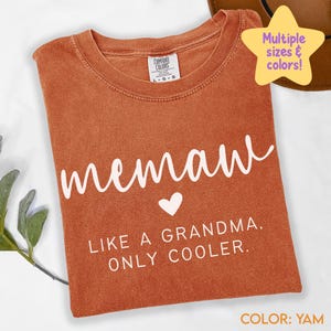 May include: A yam-colored t-shirt with the word "memaw" in white script, a white heart, and the phrase "LIKE A GRANDMA. ONLY COOLER." The shirt has a crew neck and a Comfort Colors tag. The image also includes a star-shaped graphic that says "Multiple sizes & colors!"