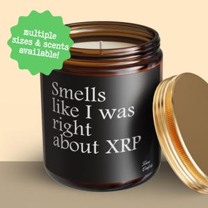 May include: A brown glass jar candle with a gold lid, featuring the text "Smells like I was right about XRP." A green sticker states "multiple sizes & scents available!"