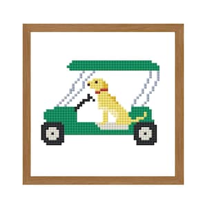 May include: A framed cross-stitch design featuring a yellow dog in a green golf cart. The dog has a red collar. The cart has black wheels and a white roof. The frame is a light brown color.