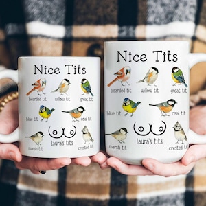 Könnte beinhalten: Zwei weiße Keramikbecher mit dem Text "Nice Tits" und Illustrationen verschiedener Vogelarten. Die Becher tragen auch den Text "Laura's tits" und die Namen der Vögel. Die Becher werden von einer Person gehalten.