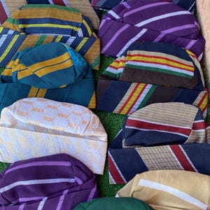 May include: A collection of colorful, patterned head wraps. The assortment includes various designs with stripes, checks, and solid colors like green, purple, and gold. These head wraps are likely for cultural or religious purposes.
