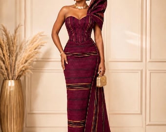 May include: A floor-length, strapless, deep burgundy gown with a corset-style bodice and a large, structured shoulder ruffle. The fabric features horizontal black and gold stripes. The text ASO GLAM EMPIRE Timeless Weave. Regal You. and DESIGN C appear.