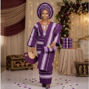 Puede incluir: Un conjunto tradicional de rayas moradas y blancas que consta de una blusa de manga larga, una falda cruzada a juego y un gran tocado. El conjunto incluye un abanico morado, un bolso de mano a juego y un collar de cuentas de coral.