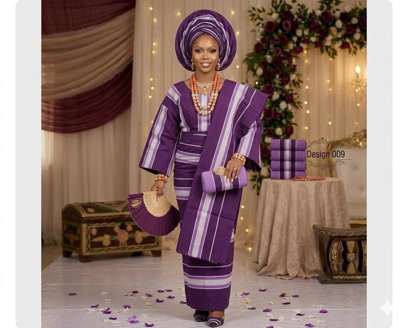 Puede incluir: Un conjunto tradicional de rayas moradas y blancas que consta de una blusa de manga larga, una falda cruzada a juego y un gran tocado. El conjunto incluye un abanico morado, un bolso de mano a juego y un collar de cuentas de coral.