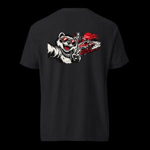 Puede incluir: Camiseta negra con un mapache de dibujos animados con gafas de sol y haciendo el signo de la paz. El diseño incluye un coche deportivo rojo, un paisaje urbano y un sol rojo en el fondo. El mapache se está haciendo un selfie.