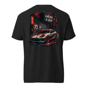 May include: A black t-shirt featuring a graphic print of a white Toyota GR 86 sports car on a city street. The design includes red and blue abstract brush strokes, Japanese text, and a sign that reads GR 86 Toyota in a dark urban setting.