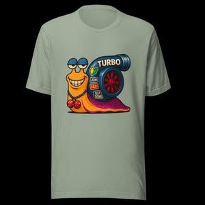May include: Sage green t-shirt featuring a cartoon snail with a turbocharger. The snail is orange with a smiling face, wearing sunglasses and a cherry necklace. The turbo has the word "TURBO" and the phrases "JDM", "FAST", and "GET SOME".