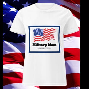 May include: White t-shirt featuring a patriotic design. The design includes an American flag within a blue border, with the words "Military Mom" and "PRAY SERVE HONOR" in black text. The background showcases an American flag.