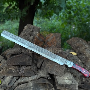Könnte beinhalten: Ein großes, verziertes Brotmesser mit gezahnter Klinge und dekorativem Muster. Der Griff ist rot und schwarz mit einem Pentagramm-Design. Das Messer wird auf einem Holzstapel präsentiert.