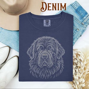 May include: Navy blue Comfort Colors sweatshirt featuring a detailed white line drawing of a Newfoundland dog's face. The word "DENIM" is in a brown script font at the top. The sweatshirt is surrounded by a hat, jeans, and white boots.