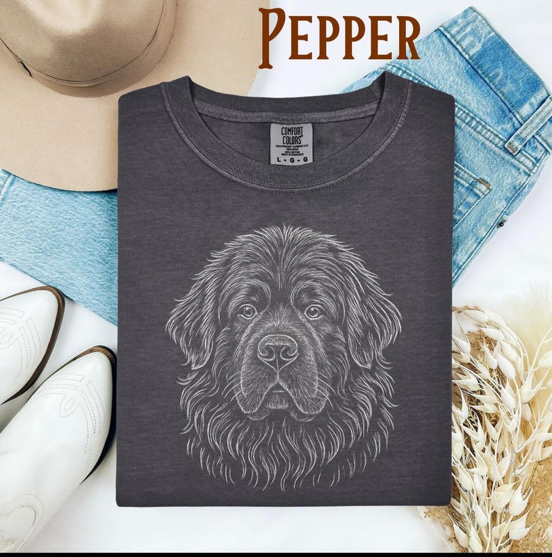 May include: Dark gray t-shirt with a detailed white line drawing of a Newfoundland dog's face. The word "PEPPER" is printed in brown at the top. The shirt is a Comfort Colors brand, and the size is L-G.