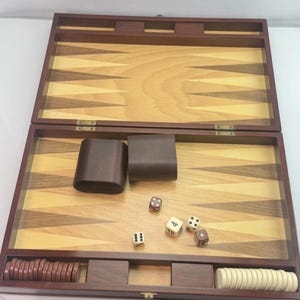 May include: Open wooden backgammon set with a dark brown frame and a light wood playing surface. Includes dice, brown leather dice cups, and wooden game pieces in brown and white.