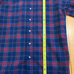 Puede incluir: Una camisa abotonada a cuadros azules, rojos y turquesas. La camisa mide aproximadamente 76 cm de largo, medida con una cinta m&eacute;trica amarilla. La camisa tiene cuello y pu&ntilde;os abotonados. La camisa est&aacute; hecha de un material suave, similar a la franela.