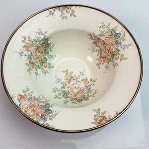 K&ouml;nnte beinhalten: Eine runde Keramikschale mit cremefarbener Basis und einem Blumenmuster aus hellrosa Rosen und kleinen blauen Bl&uuml;ten. Die Schale hat einen d&uuml;nnen, dunkelmetallischen Rand, und die Innenfl&auml;che ist mit drei verschiedenen Blumenarrangements verziert.