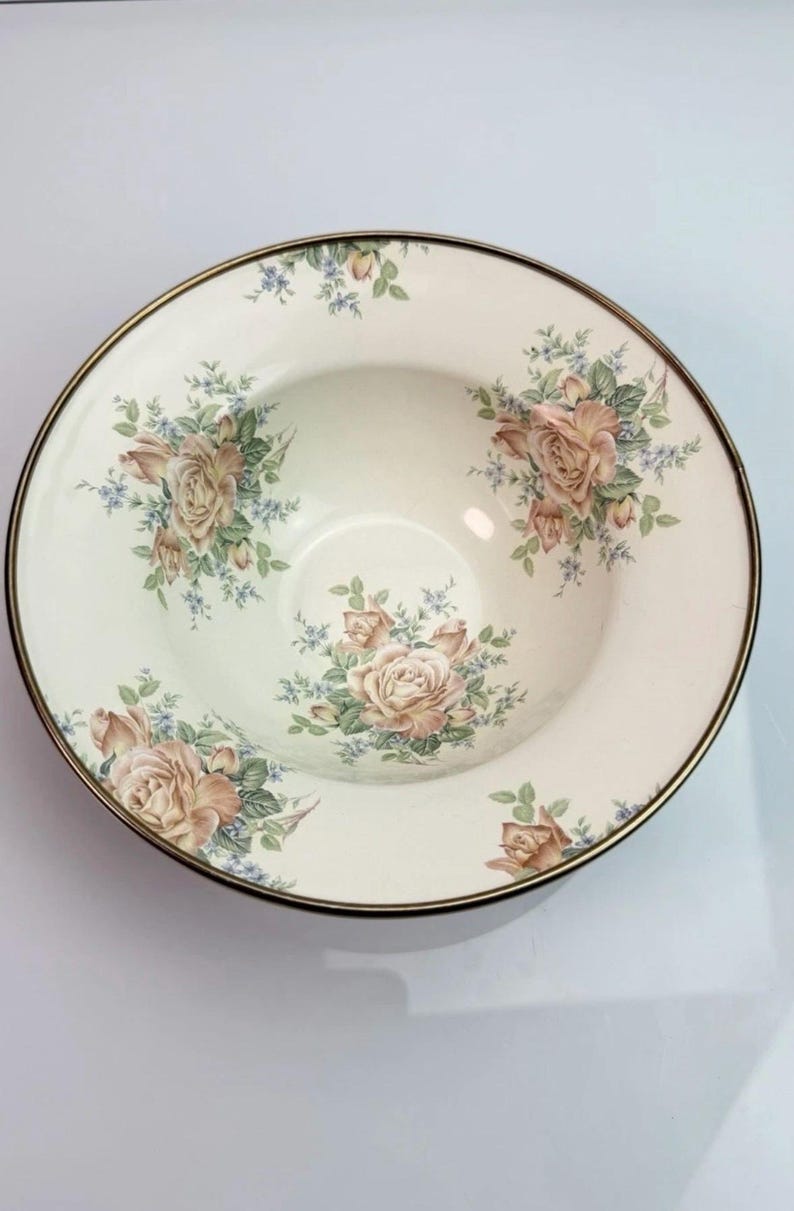K&ouml;nnte beinhalten: Eine runde Keramikschale mit cremefarbener Basis und einem Blumenmuster aus hellrosa Rosen und kleinen blauen Bl&uuml;ten. Die Schale hat einen d&uuml;nnen, dunkelmetallischen Rand, und die Innenfl&auml;che ist mit drei verschiedenen Blumenarrangements verziert.